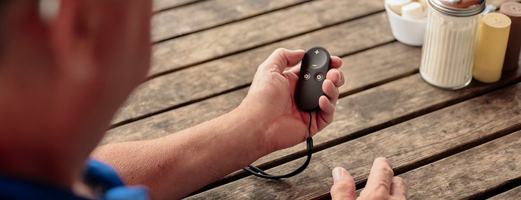 Image of male hearing aid wearer holding a Hearing Aid Remote 2.0 at a table